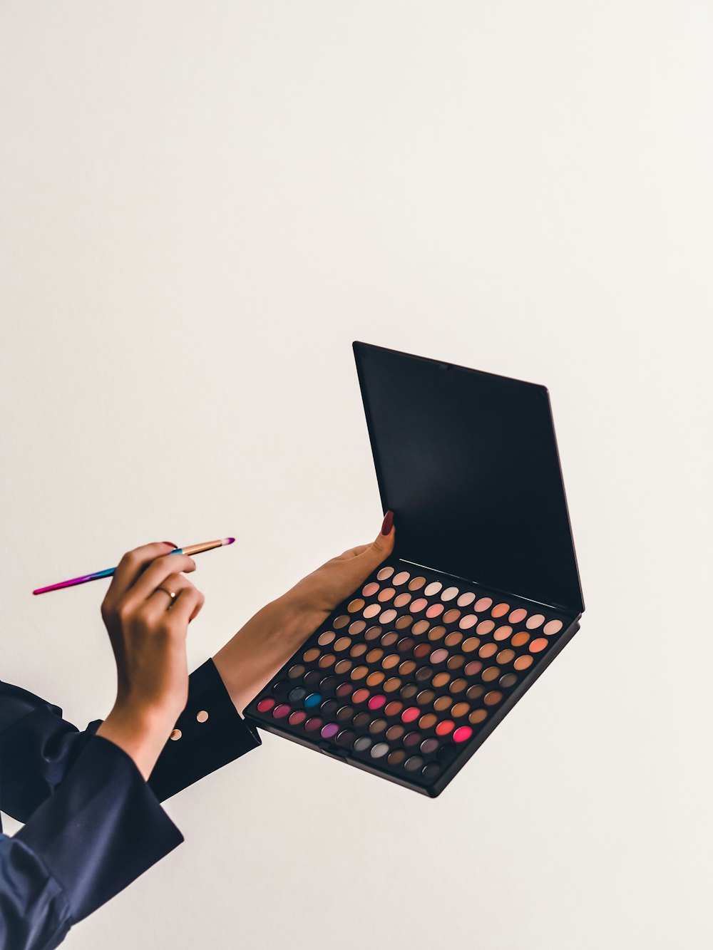 Mano sujetando una paleta de sombras de ojos y un pincel