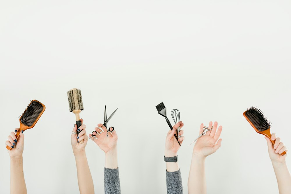 Varias manos sosteniendo cepillos, tijeras y herramientas de peluquería