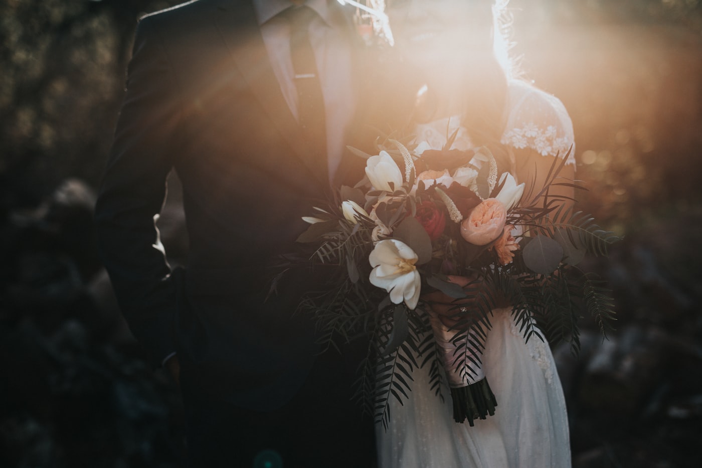 Novia con vestido blanco sosteniendo un ramo de flores a contraluz