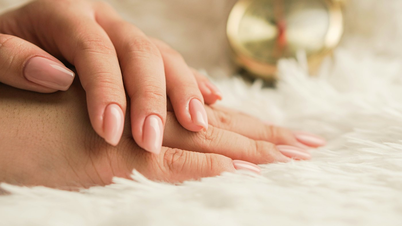 Manos con manicura en tono nude apoyadas sobre una manta blanca