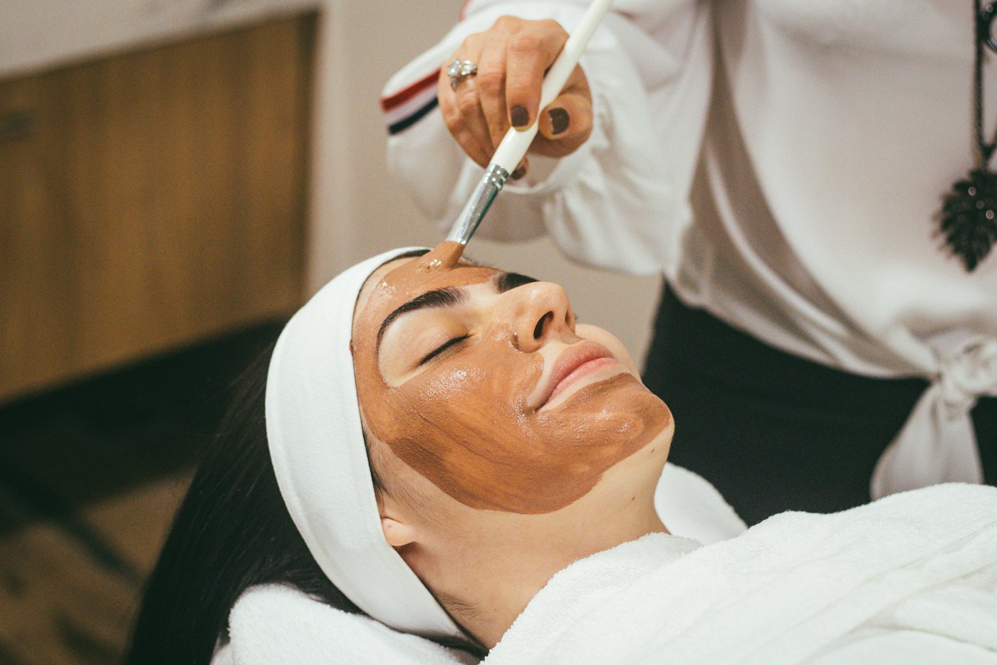 Clienta con los ojos cerrados mientras le aplican una mascarilla facial con pincel